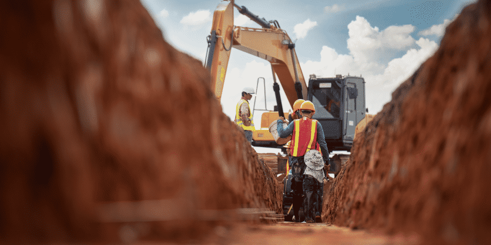 Professional construction workers in excavation trench with excavator, demonstrating teamwork and controlled execution on construction site